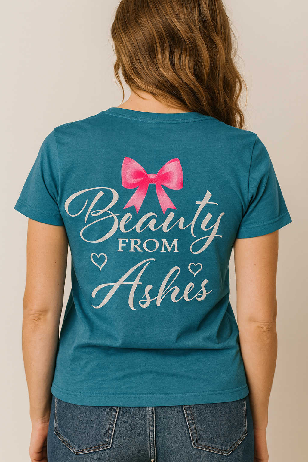Teal t-shirt with a pink bow and 'Beauty from Ashes' text on the back, worn by a person.