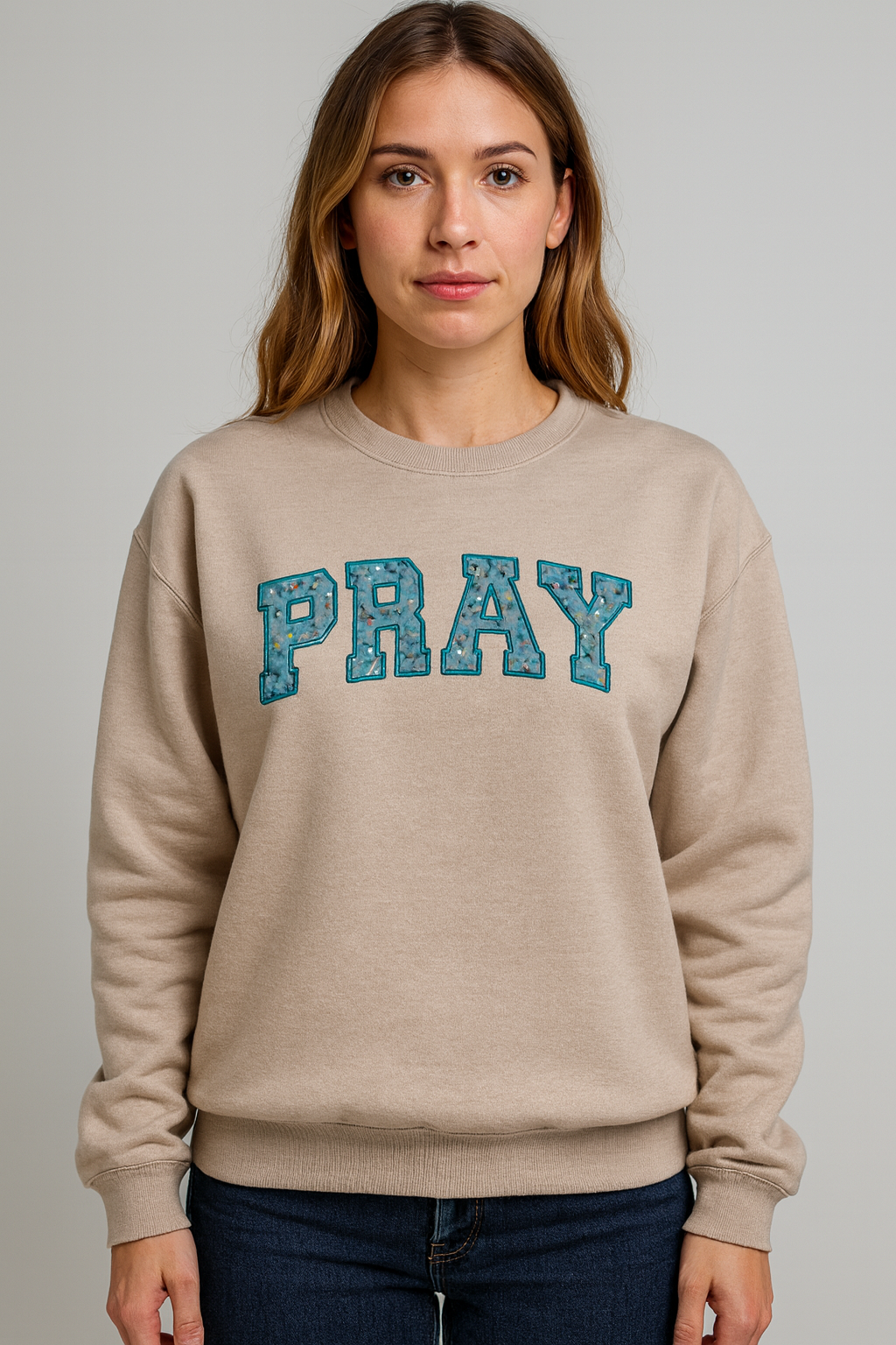 Person wearing a sand colored sweatshirt with 'PRAY' embroidered on ladies sweatshirt.