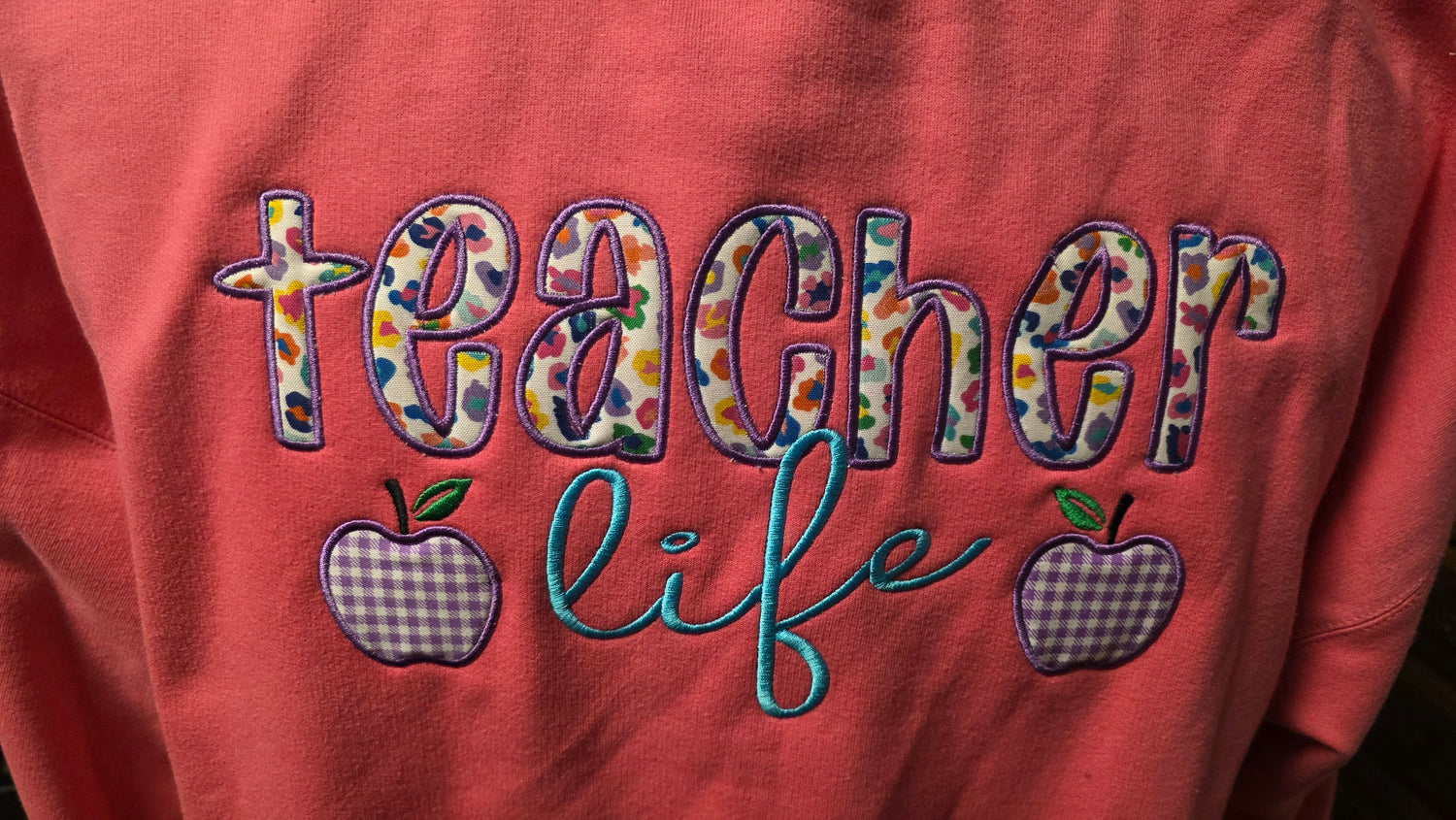 Pink sweatshirt with 'teacher life' text and apple graphics on a red background