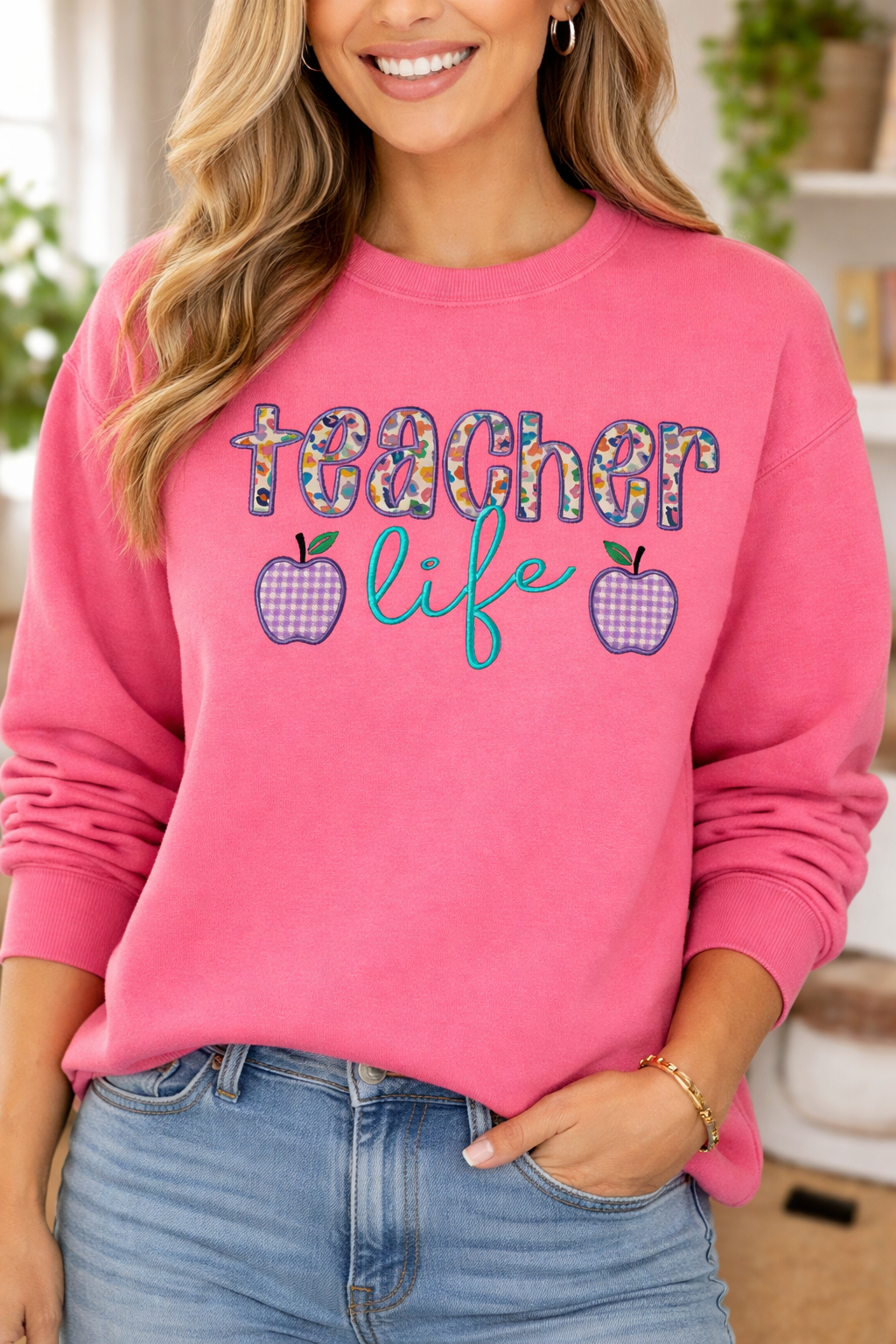 Person wearing a pink sweatshirt with 'teacher life' text and apple graphics.